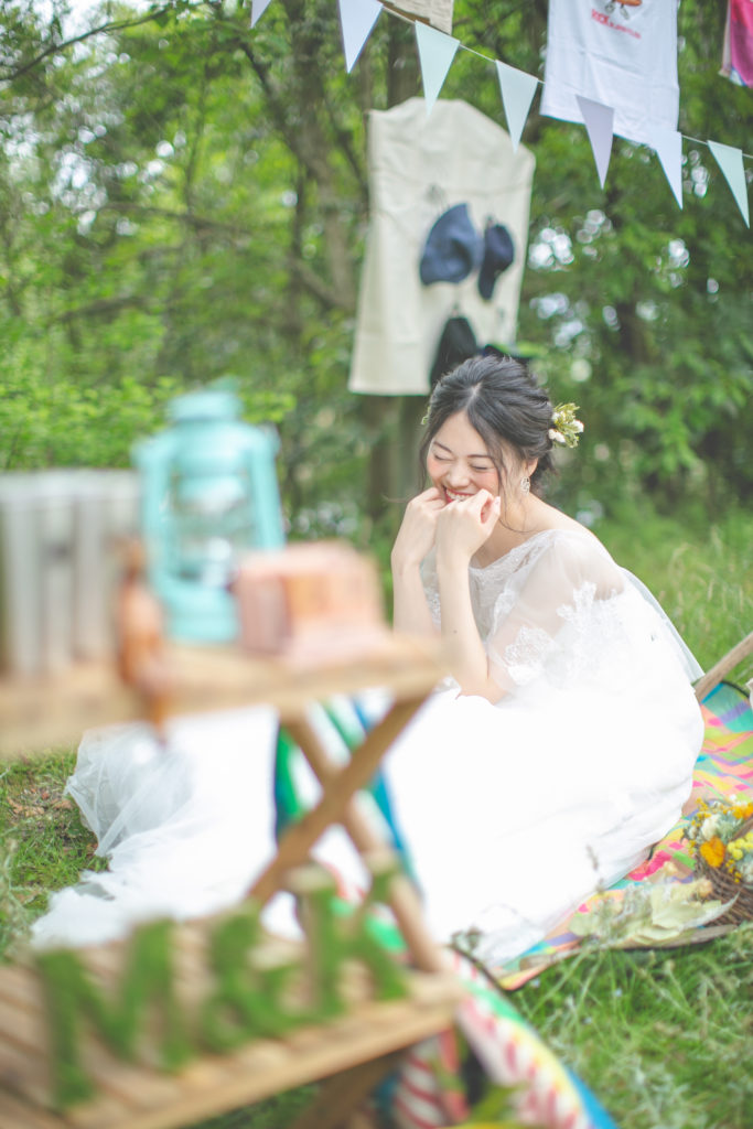 ピクニック風のフォトウェディングで手を顔に当てながら笑う新婦