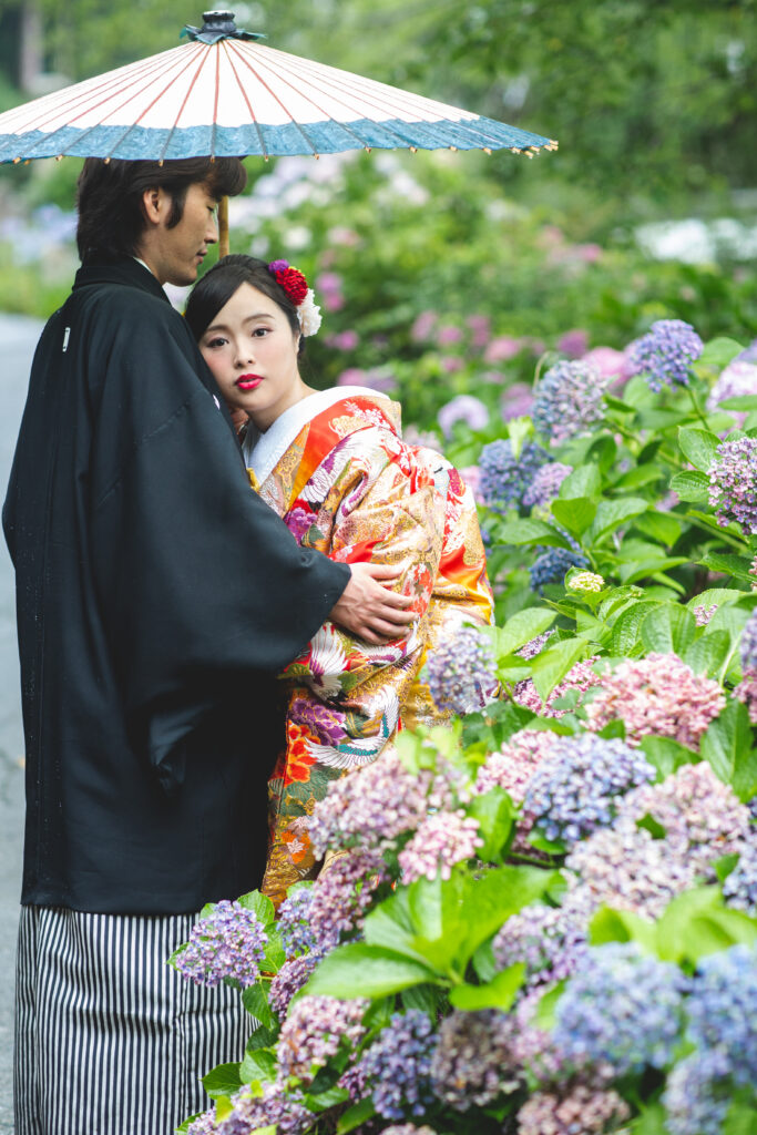 紫陽花の前で傘をさしてたたずむ和装の新郎新婦