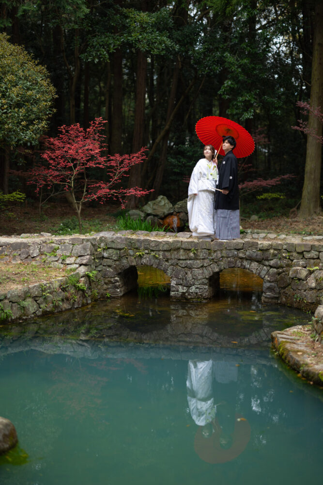 大麻比古神社のめがね橋の上で赤い傘をさしている新郎新婦