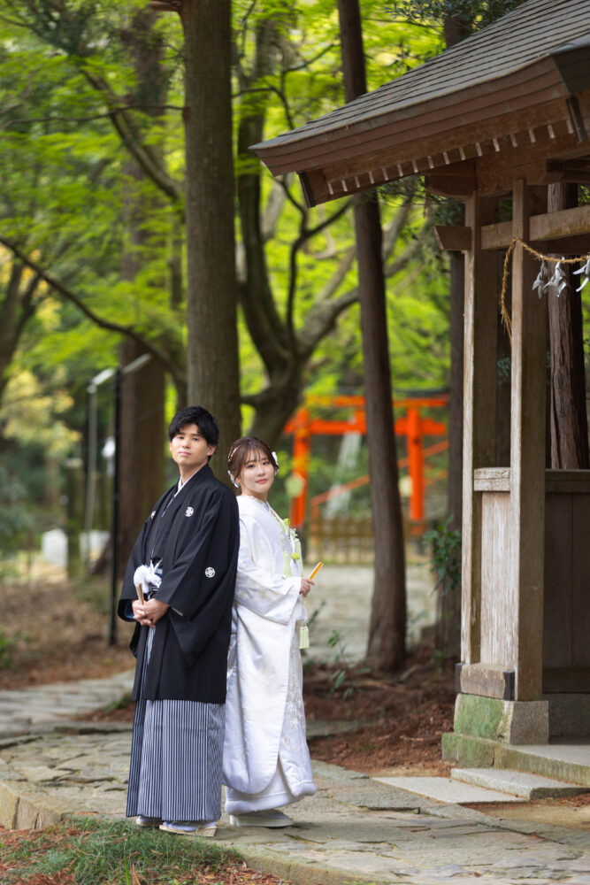 鳥居をバックに和装姿で立つ新郎新婦