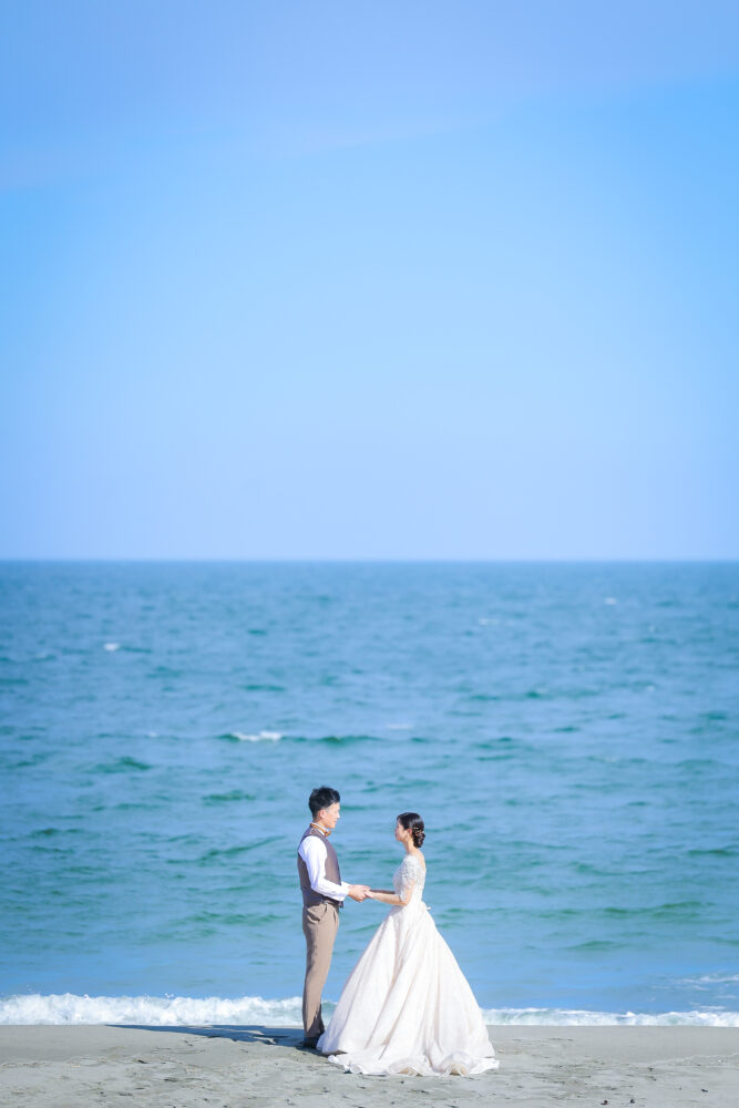 青空と海をバックに向かい合う新郎新婦